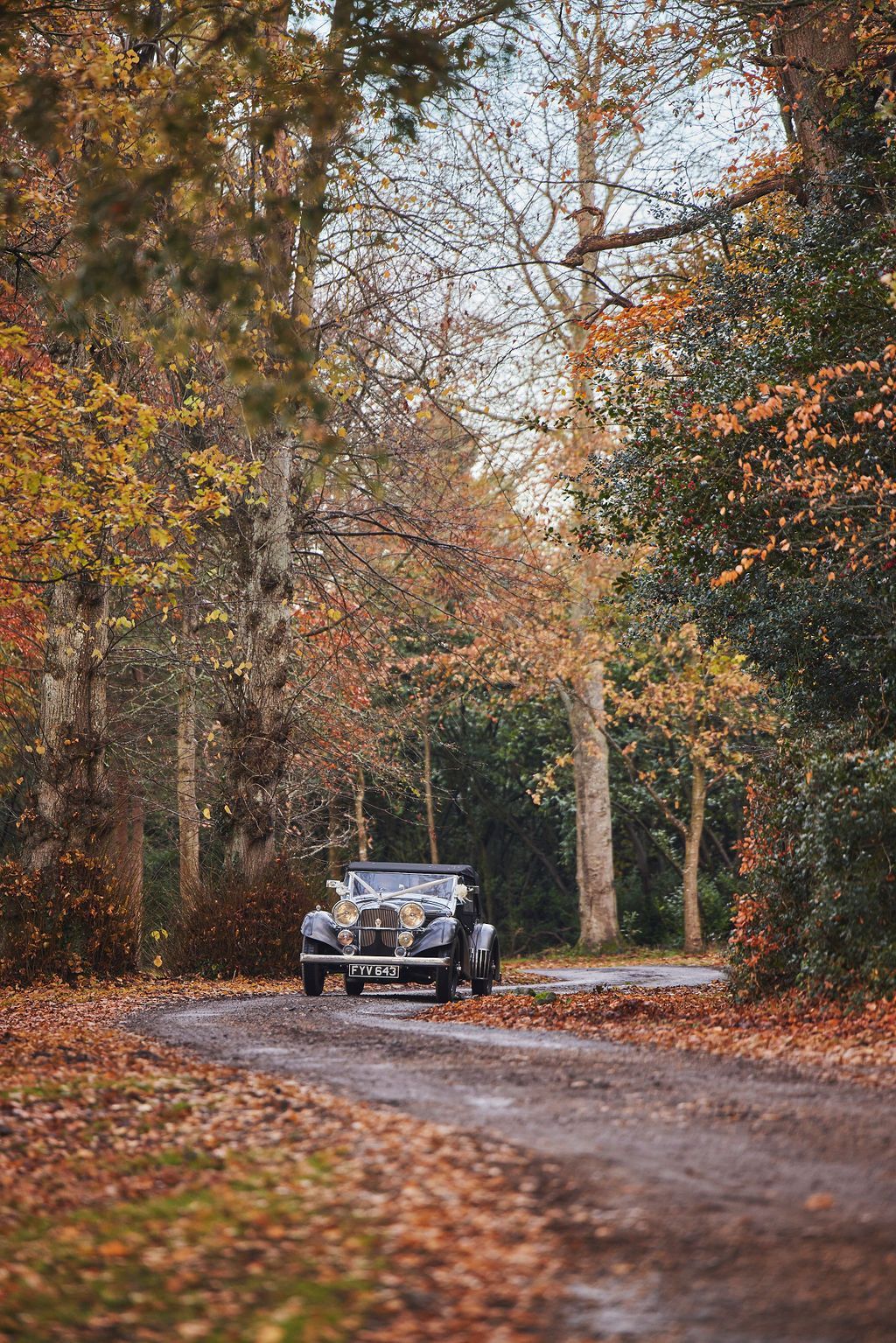 a black car is driving down a dirt road surrounded by trees.
