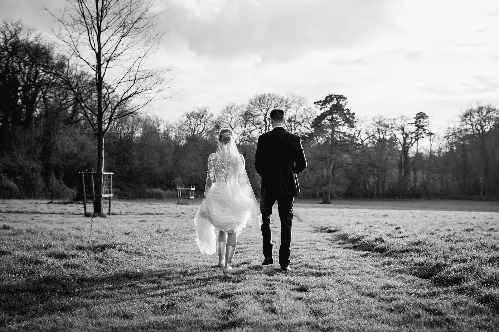 a black and white photo of a bride and groom walking in a field .