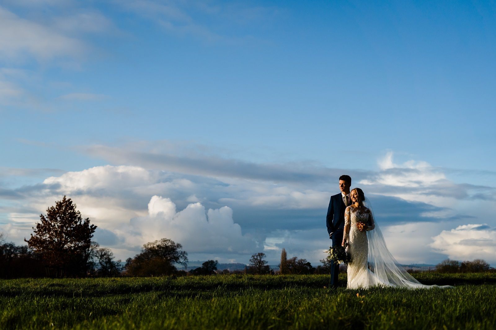 a bride and groom are standing in a grassy field .
