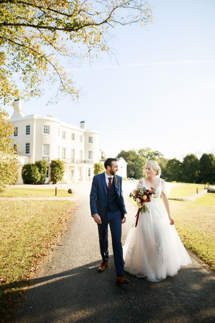 a bride and groom are walking down a path in front of a large white building.
