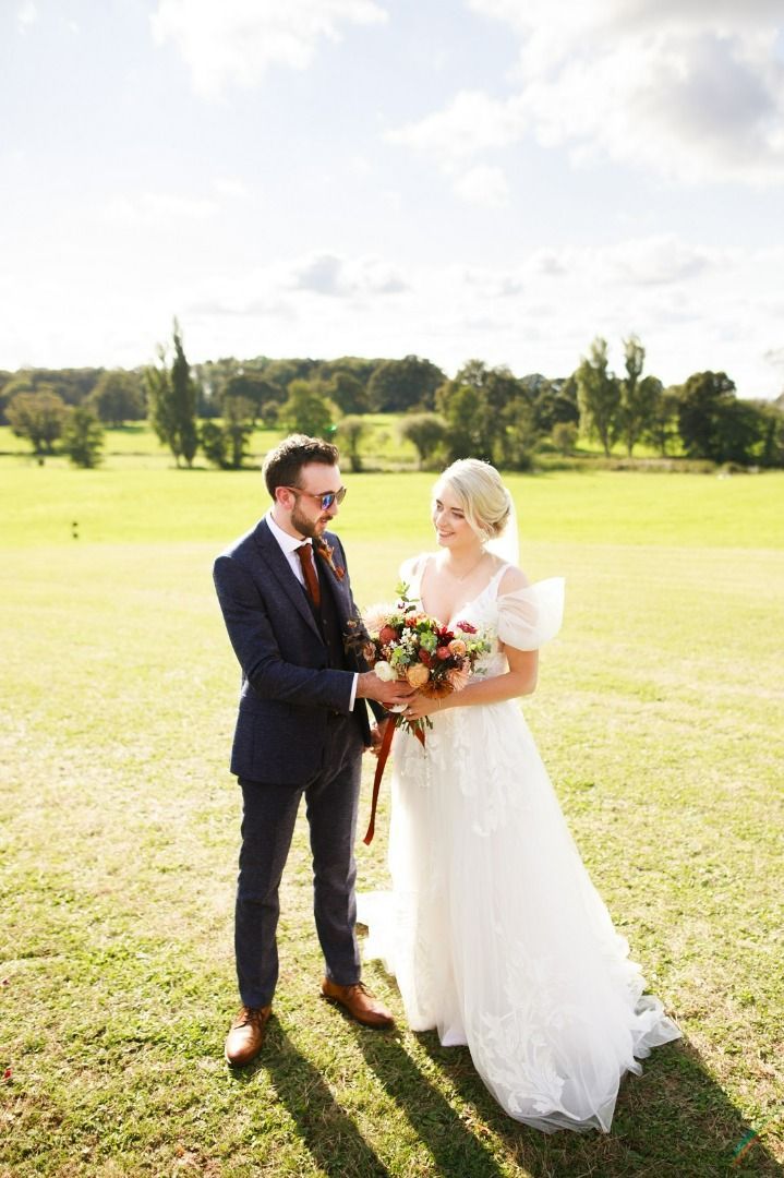 a bride and groom are standing in a field holding hands.