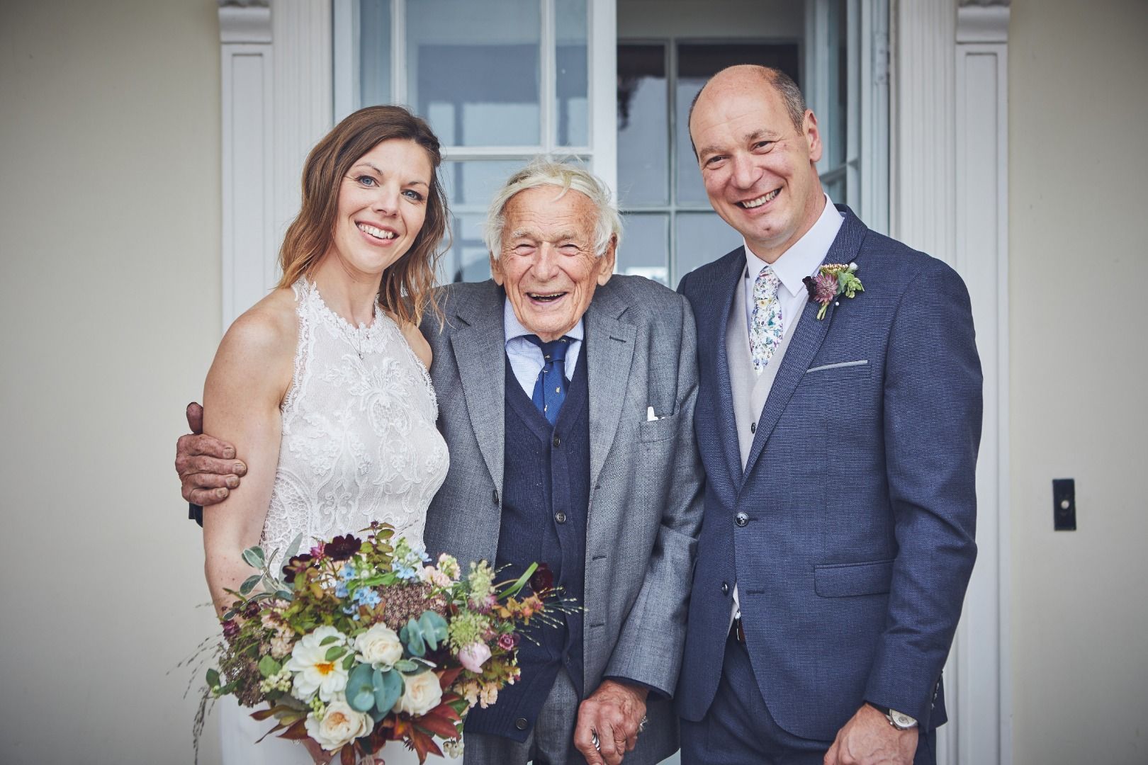 a bride and groom are posing for a picture with their grandfather .