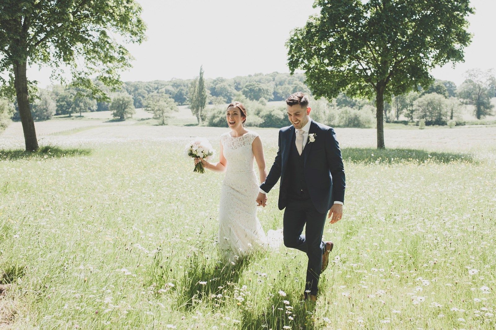 a bride and groom are walking through a field holding hands .