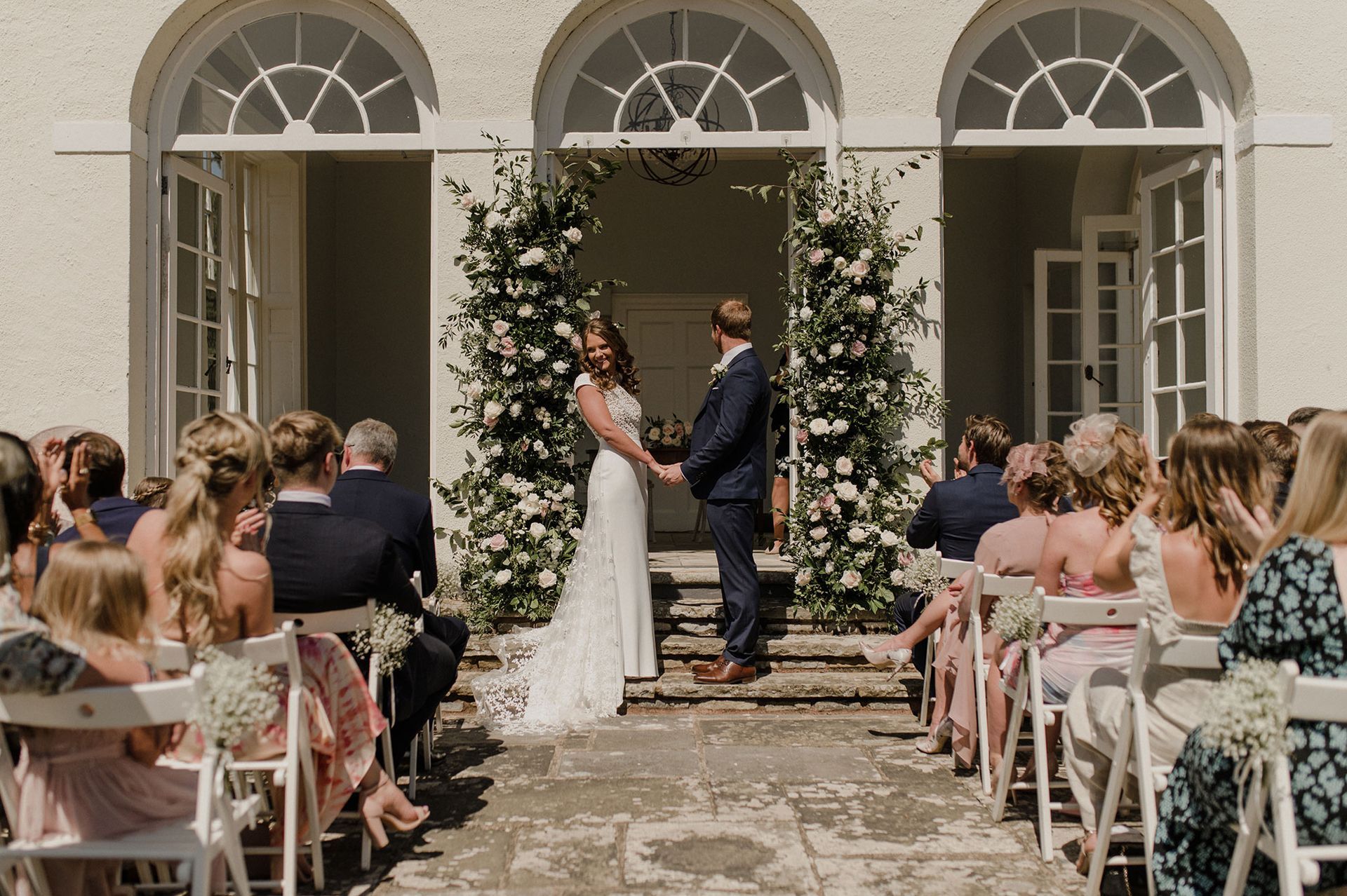 a bride and groom are holding hands during their wedding ceremony while their guests watch .
