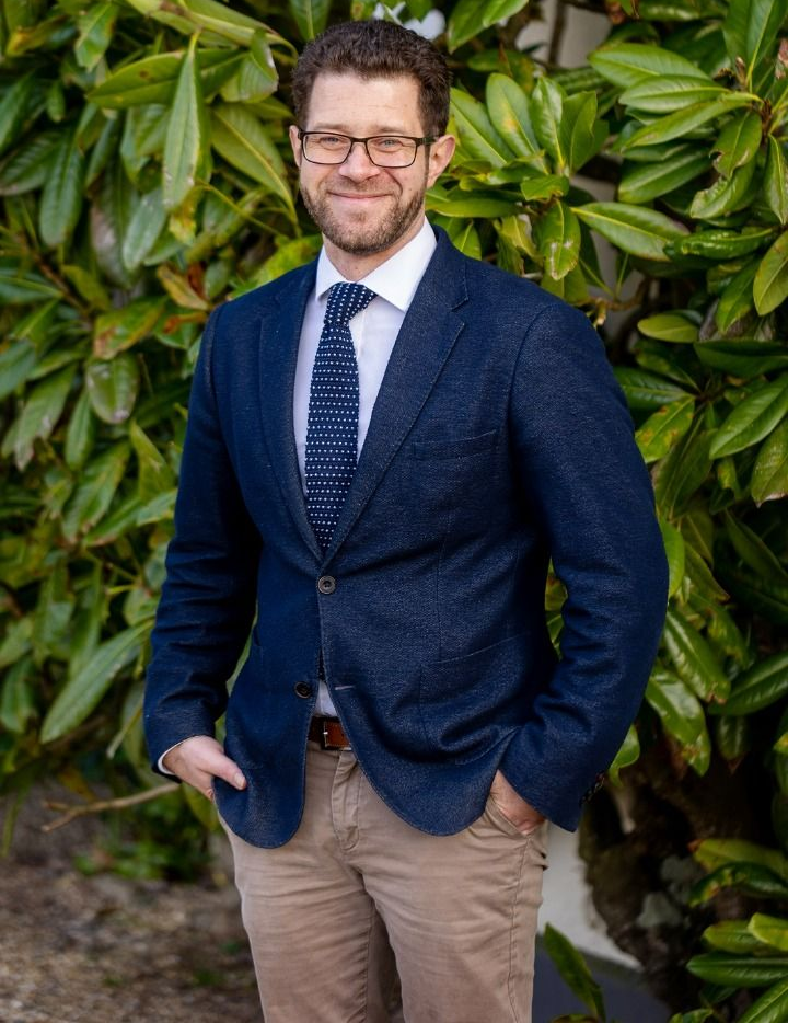 a man in a suit and tie is standing in front of a bush .