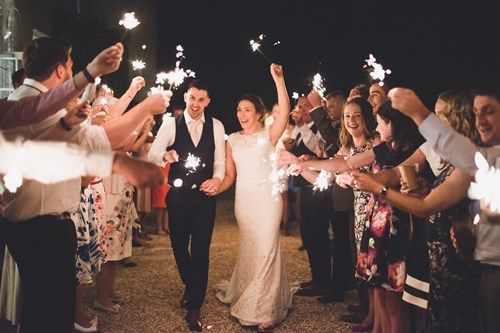 a bride and groom are walking through a tunnel of sparklers .