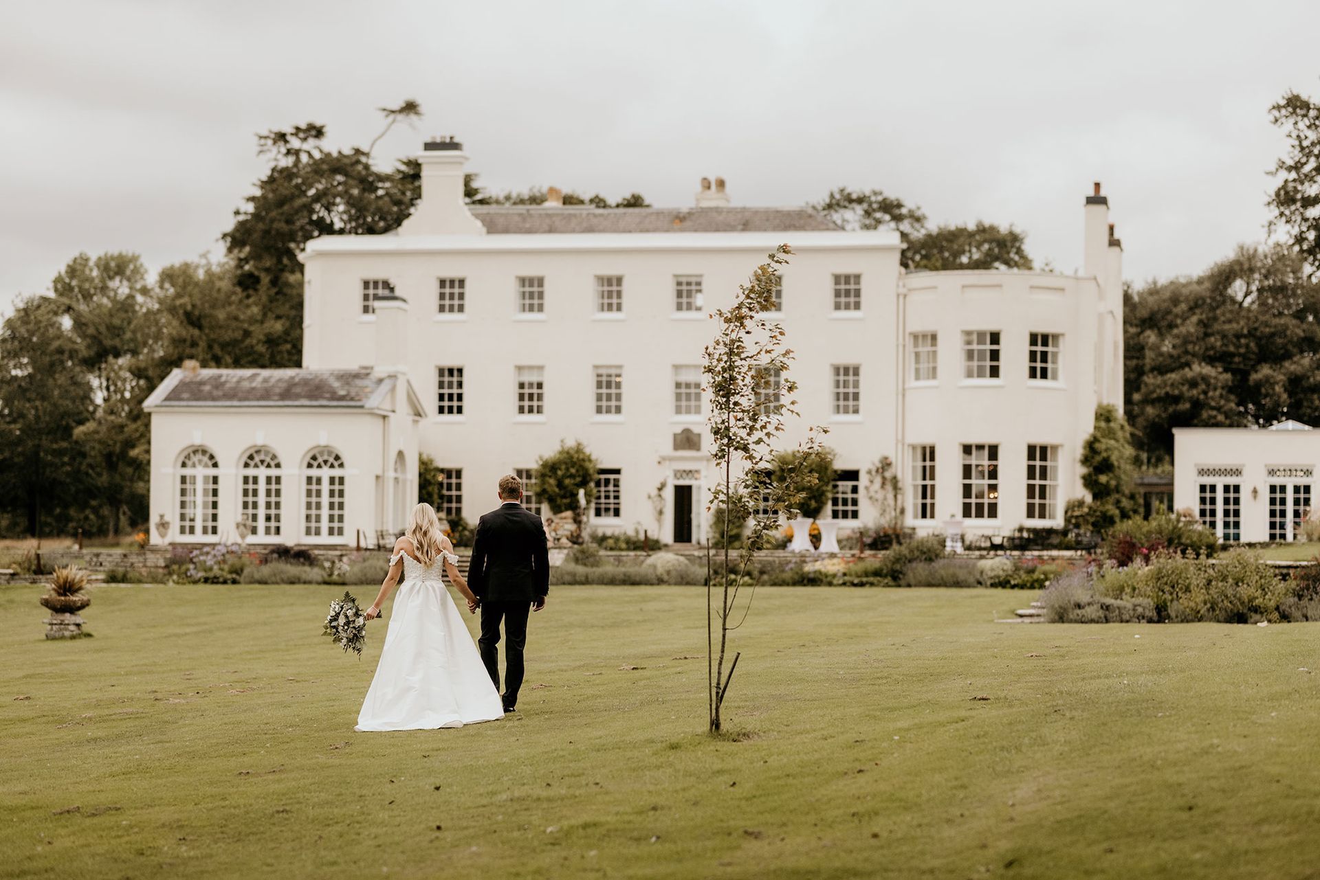 a bride and groom are walking in front of a large white house .