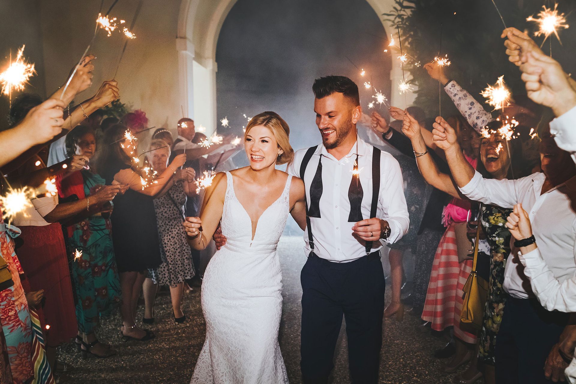 a bride and groom are walking through a tunnel of sparklers .
