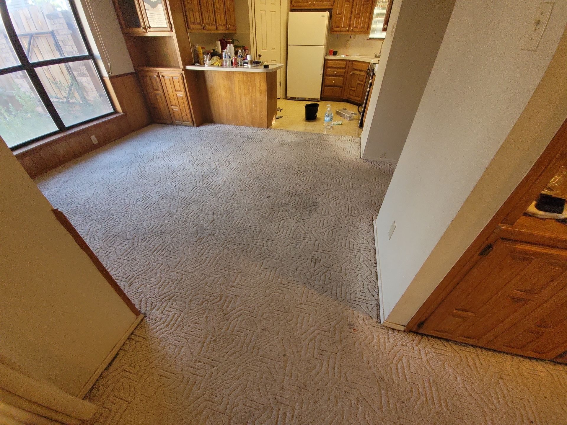 A room with a carpeted floor and a kitchen in the background