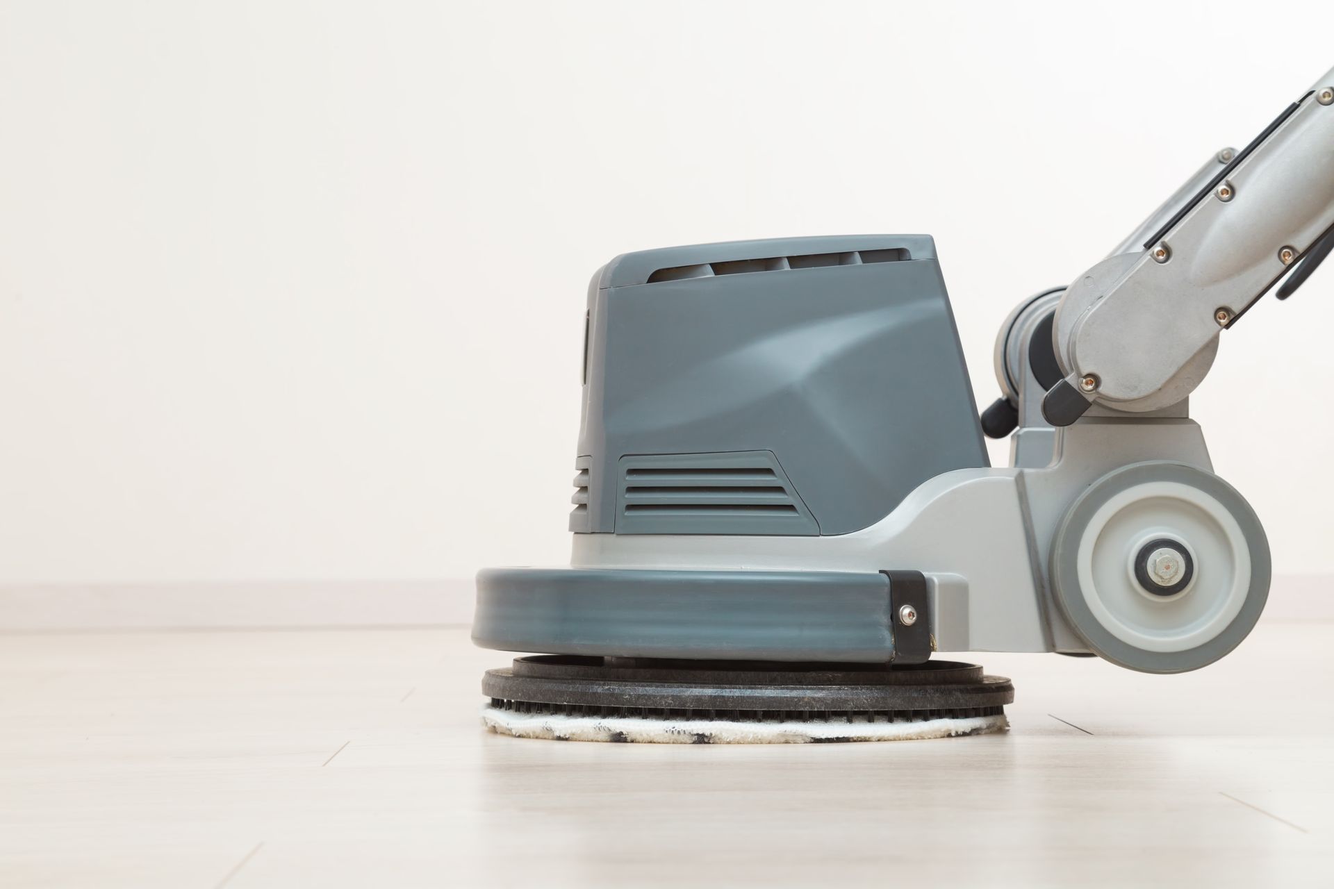 Floor buffer machine cleaning a light wood floor in a bright room
