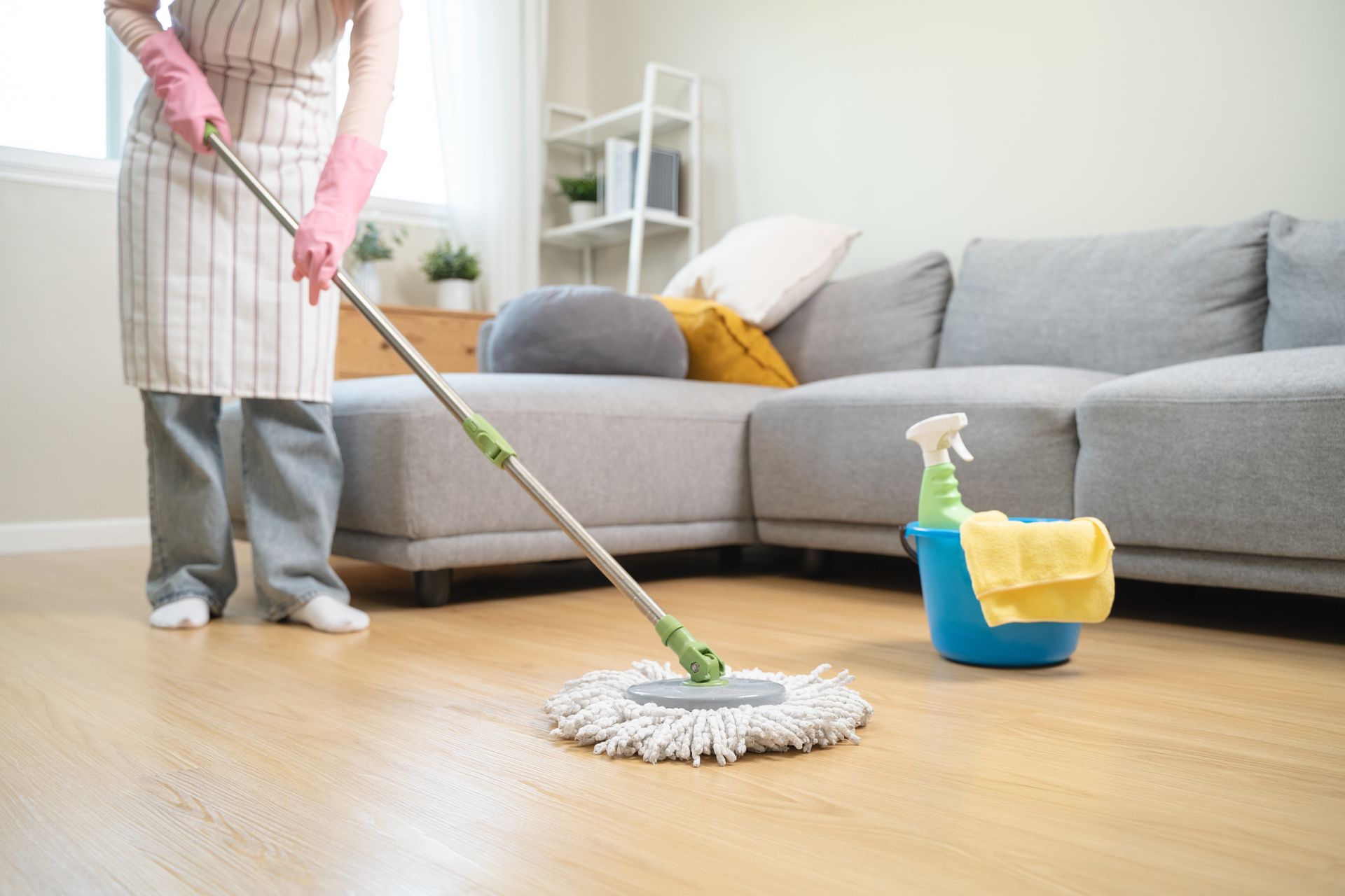 Person mopping a hardwood floor in a bright living room, with cleaning supplies nearby.