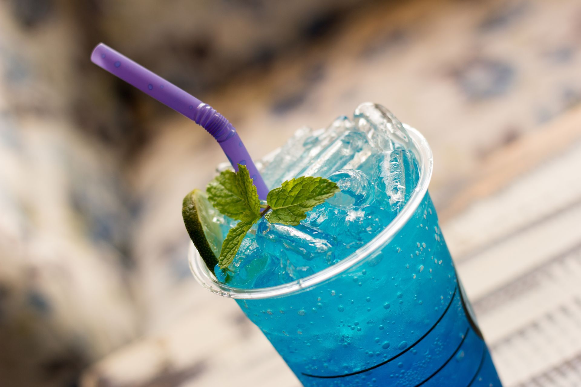 Blue drink in a clear plastic cup with ice, straw, and mint garnish.