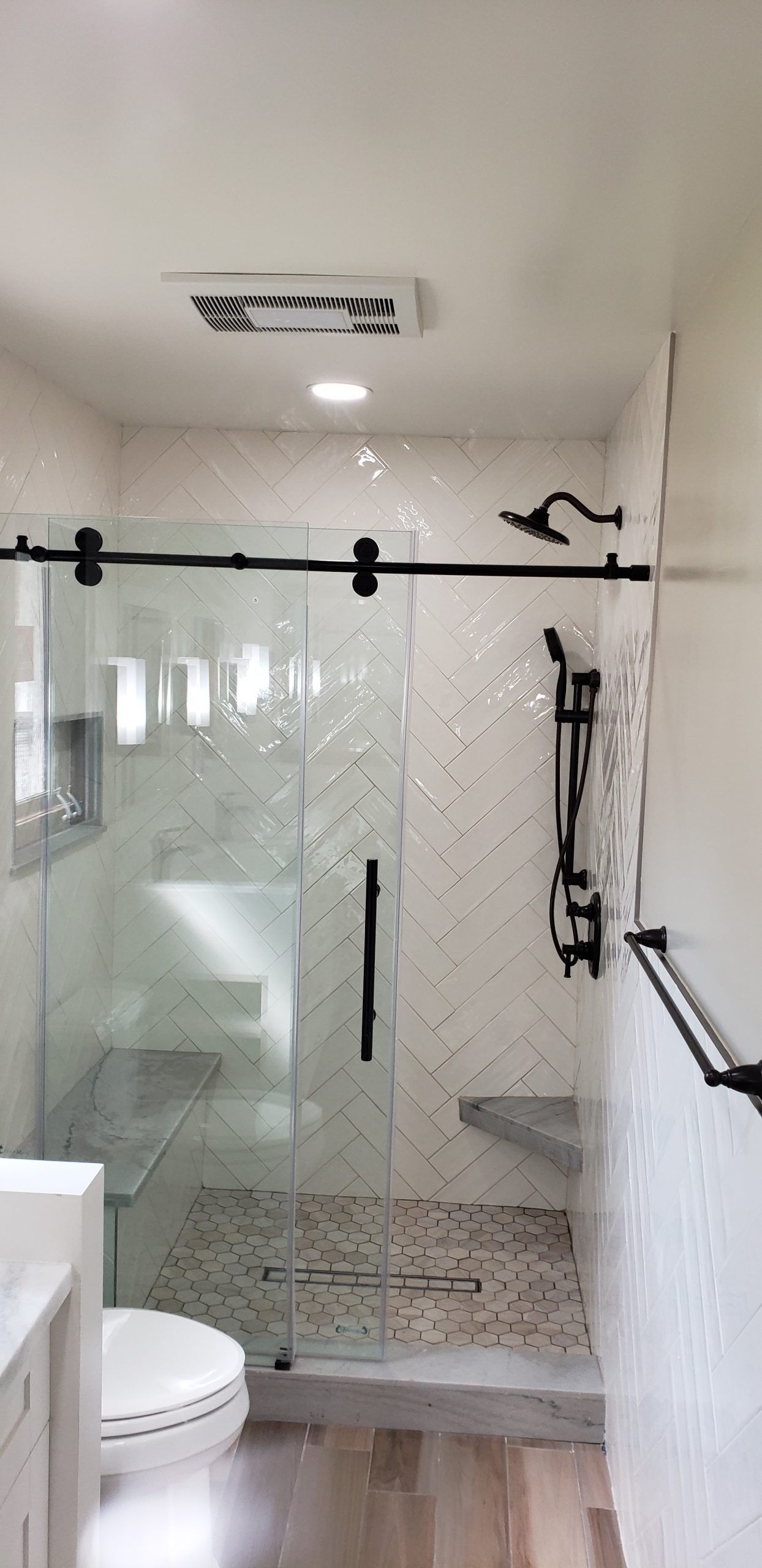 A bathroom with a toilet and a shower with a sliding glass door from a Bathroom remodel in San Diego CA by Team Renovate