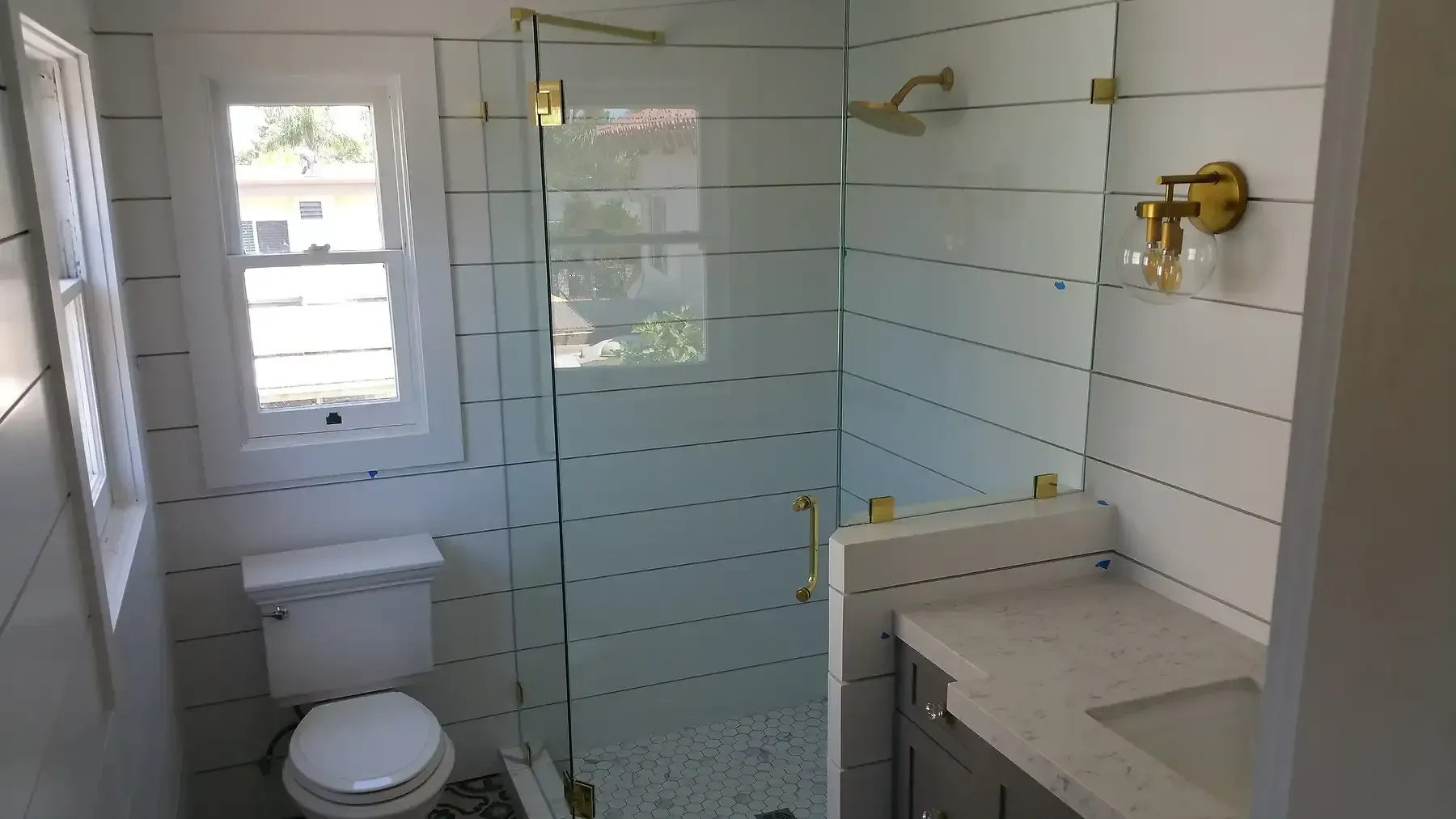 A bathroom with a toilet , sink , shower and window gold accents in Point Loma