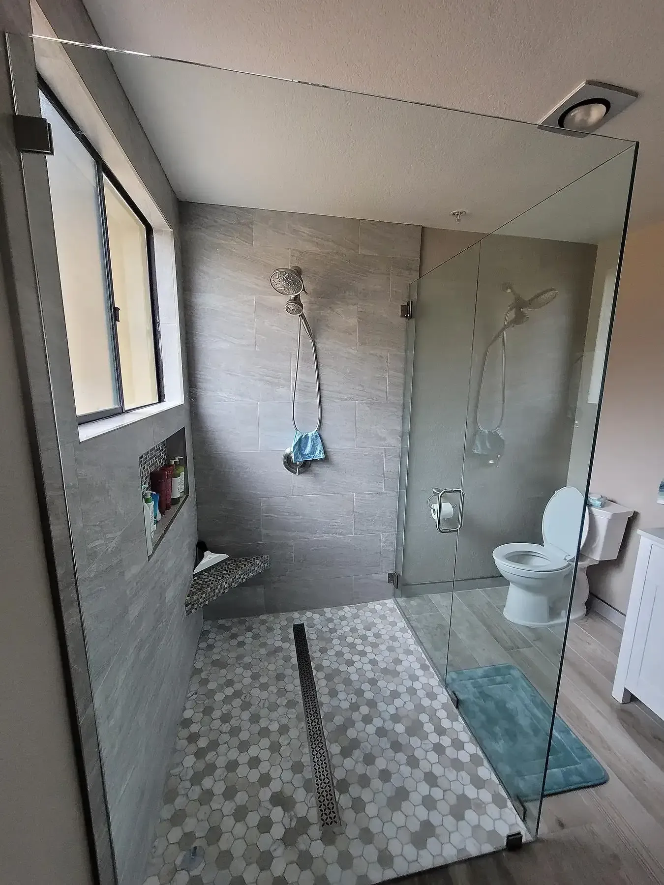 A bathroom with a walk in shower , toilet and window.