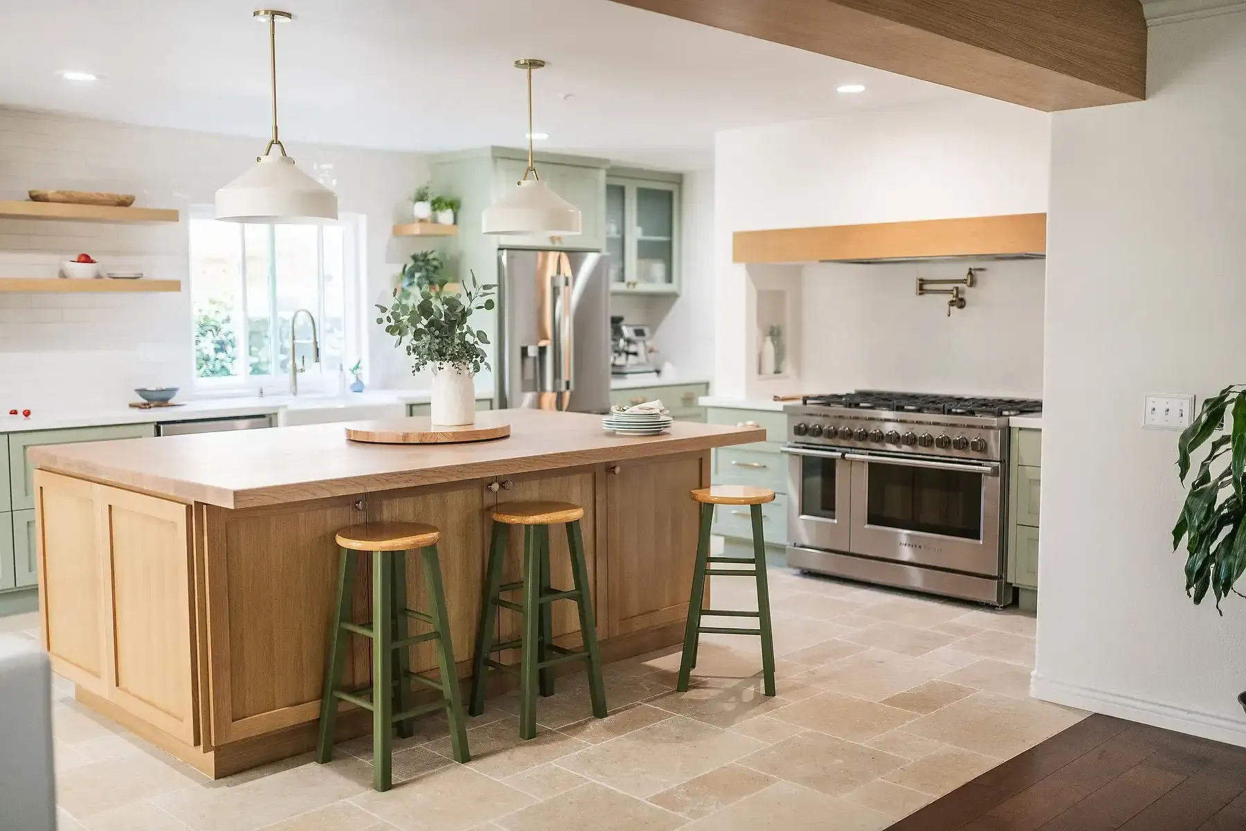 Team Renovate - Spacious kitchen with wood island, green stools, stainless steel appliances, and sage green cabinetry.