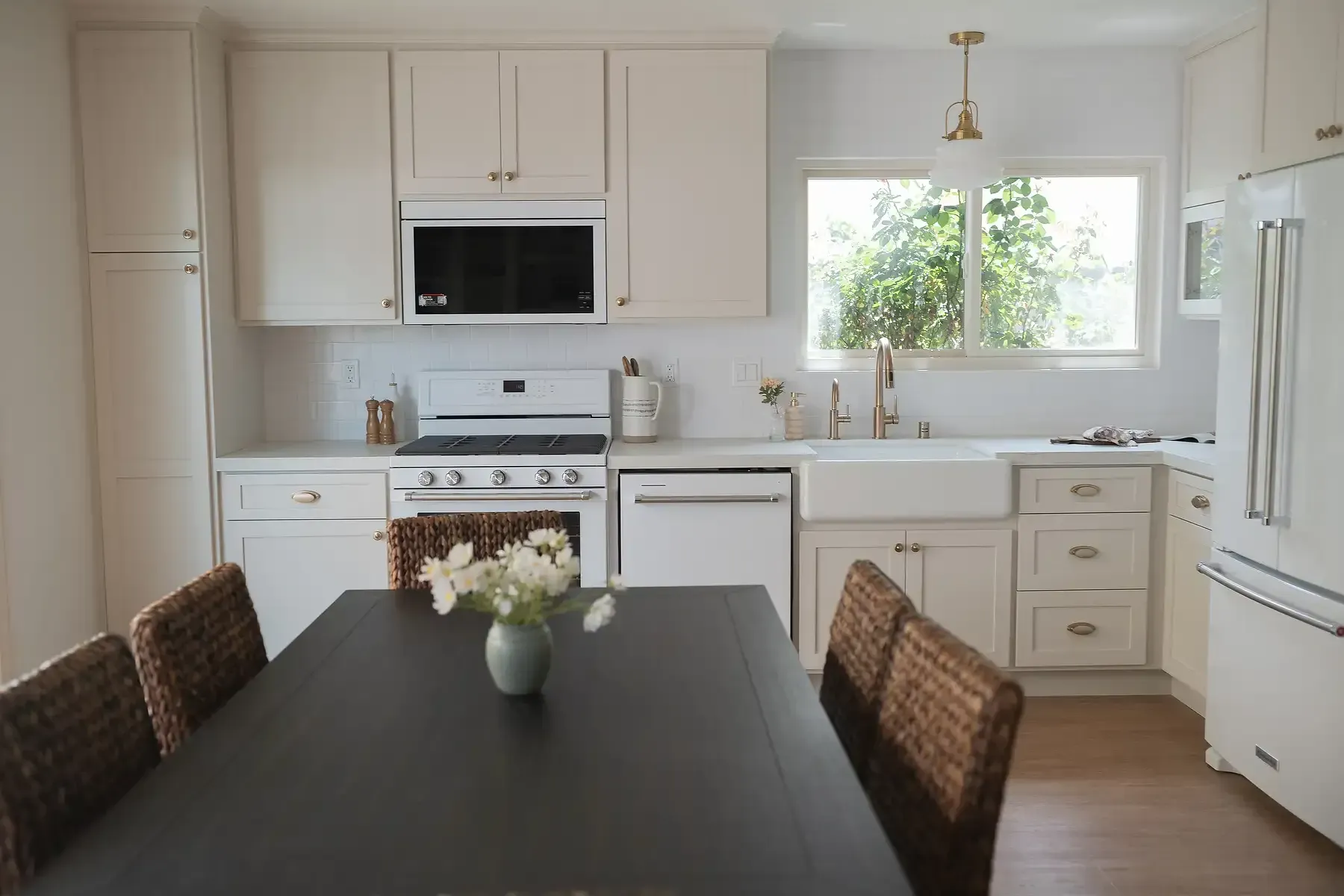 Team Renovate - White kitchen with cabinets, appliances, and a dark table with woven chairs.
