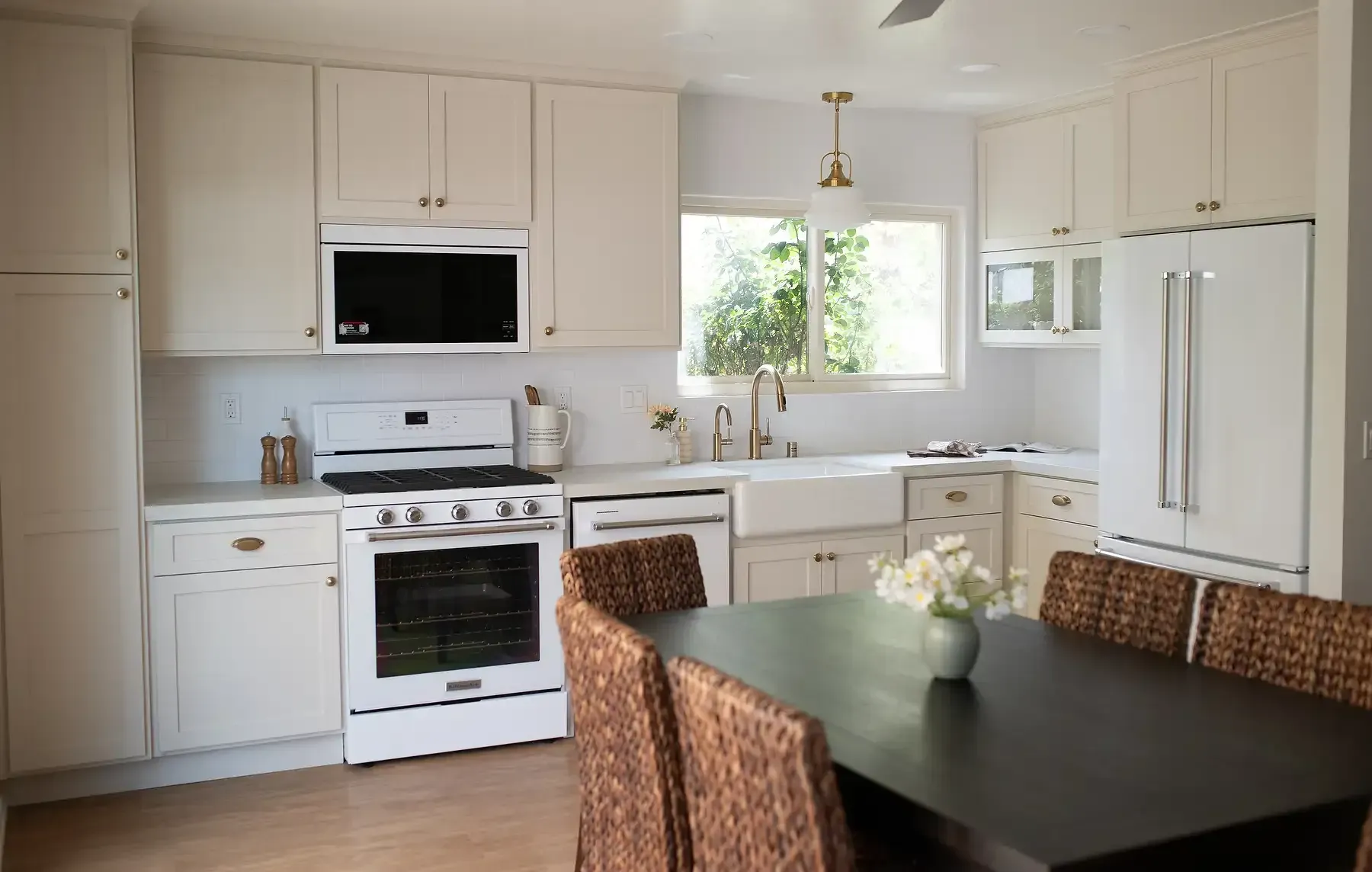 Team Renovate - White kitchen with white cabinets, appliances, and a dark table with wicker chairs.