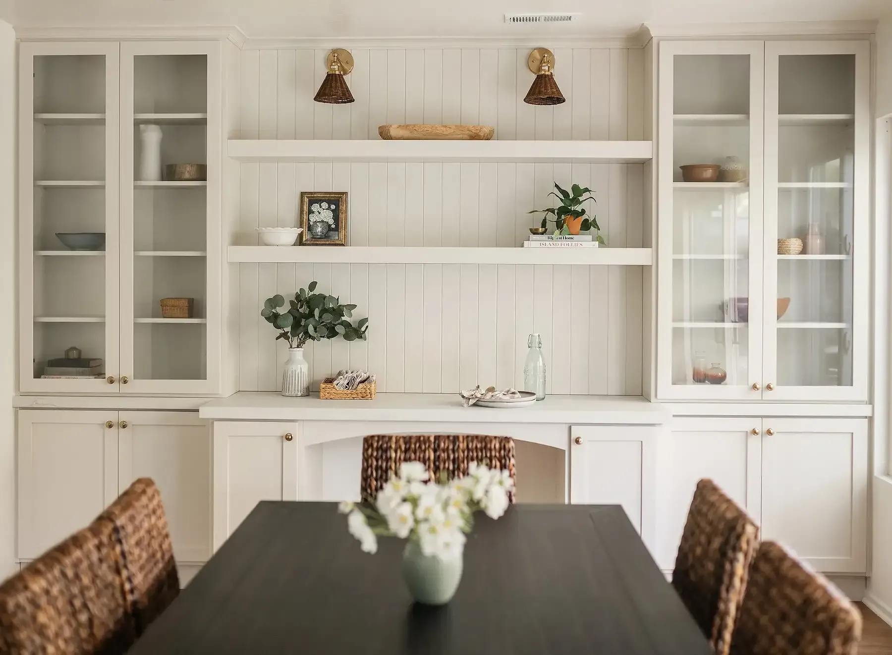 Team Renovate - Dining room with built-in white shelves, glass-door cabinets, dark table, and woven chairs.