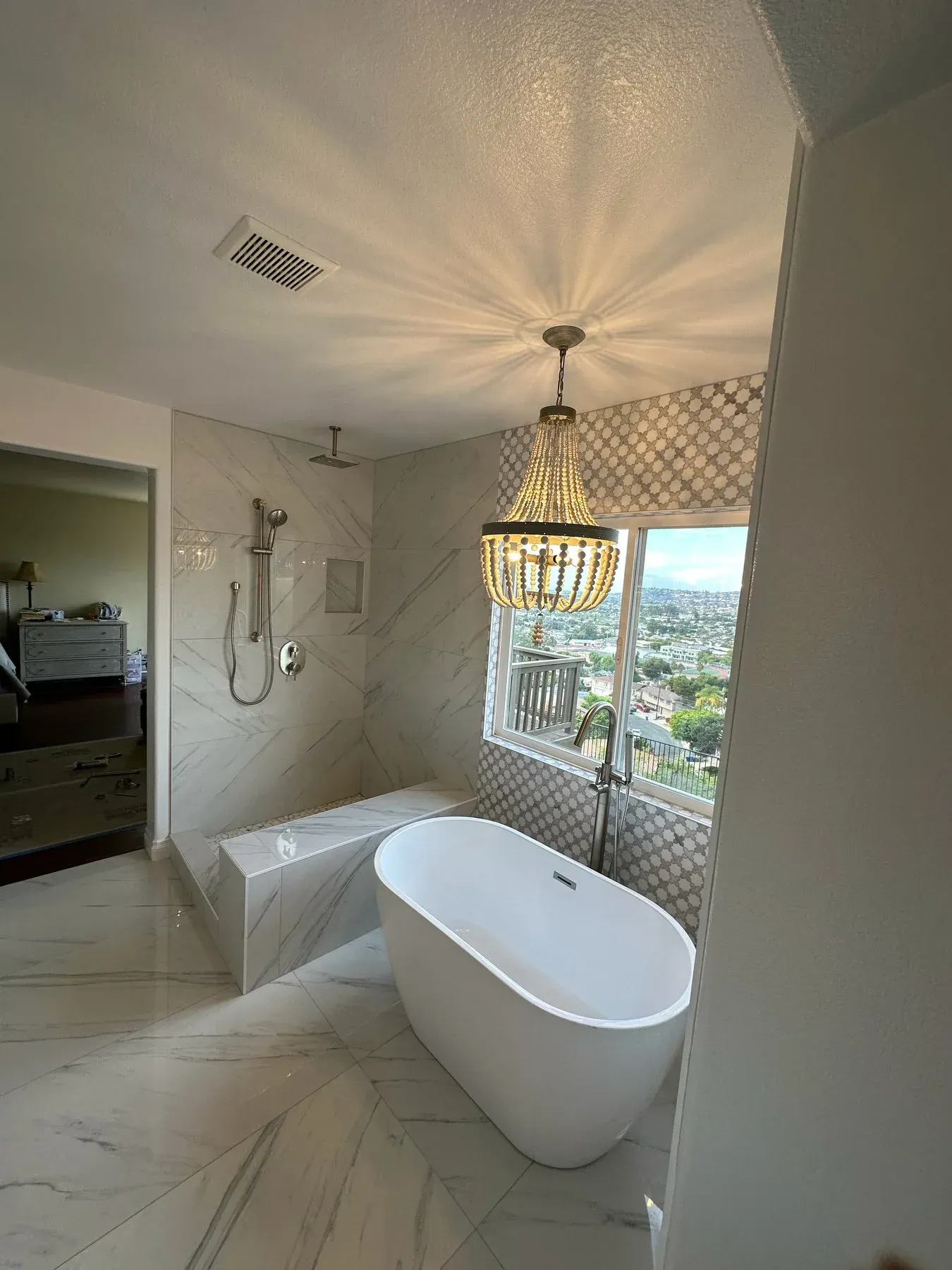 A bathroom with a bathtub , shower , and chandelier from a Bathroom remodel in San Diego CA by Team Renovate