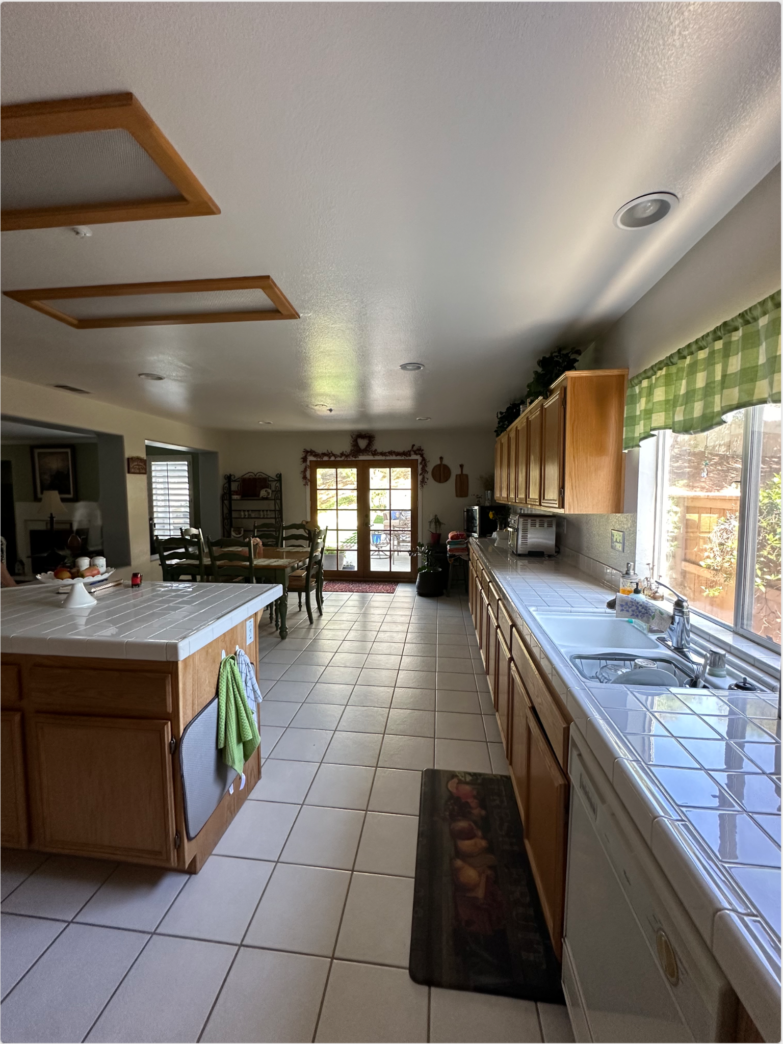Team Renovate - Long kitchen with light wood cabinets, white countertops, tile floors, and a view to the backyard.