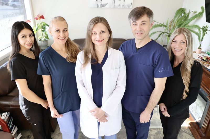 Five healthcare staff posing together in a bright clinic, wearing scrubs and a white lab coat