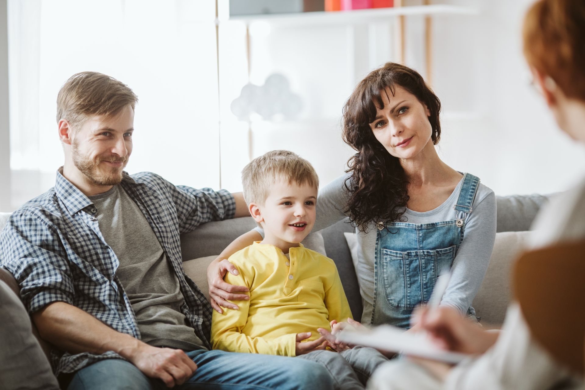 Family sitting together on a couch in a bright living room, with a child pointing forward.