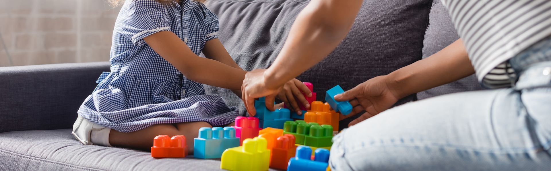 Hands stacking colorful blocks on a gray couch