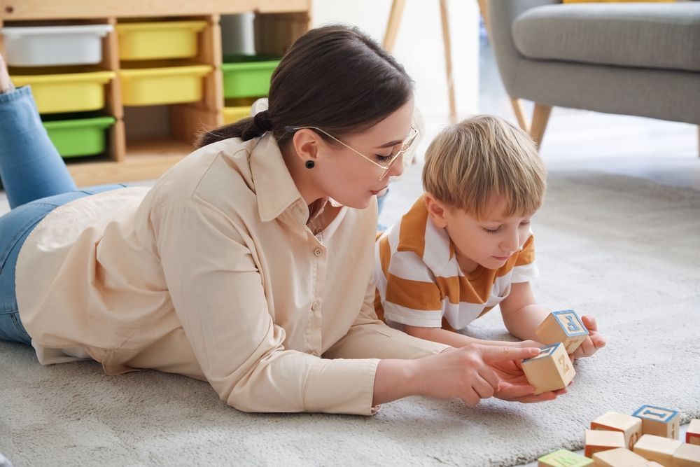 Adult and child playing with wooden blocks on a carpet in a bright living room