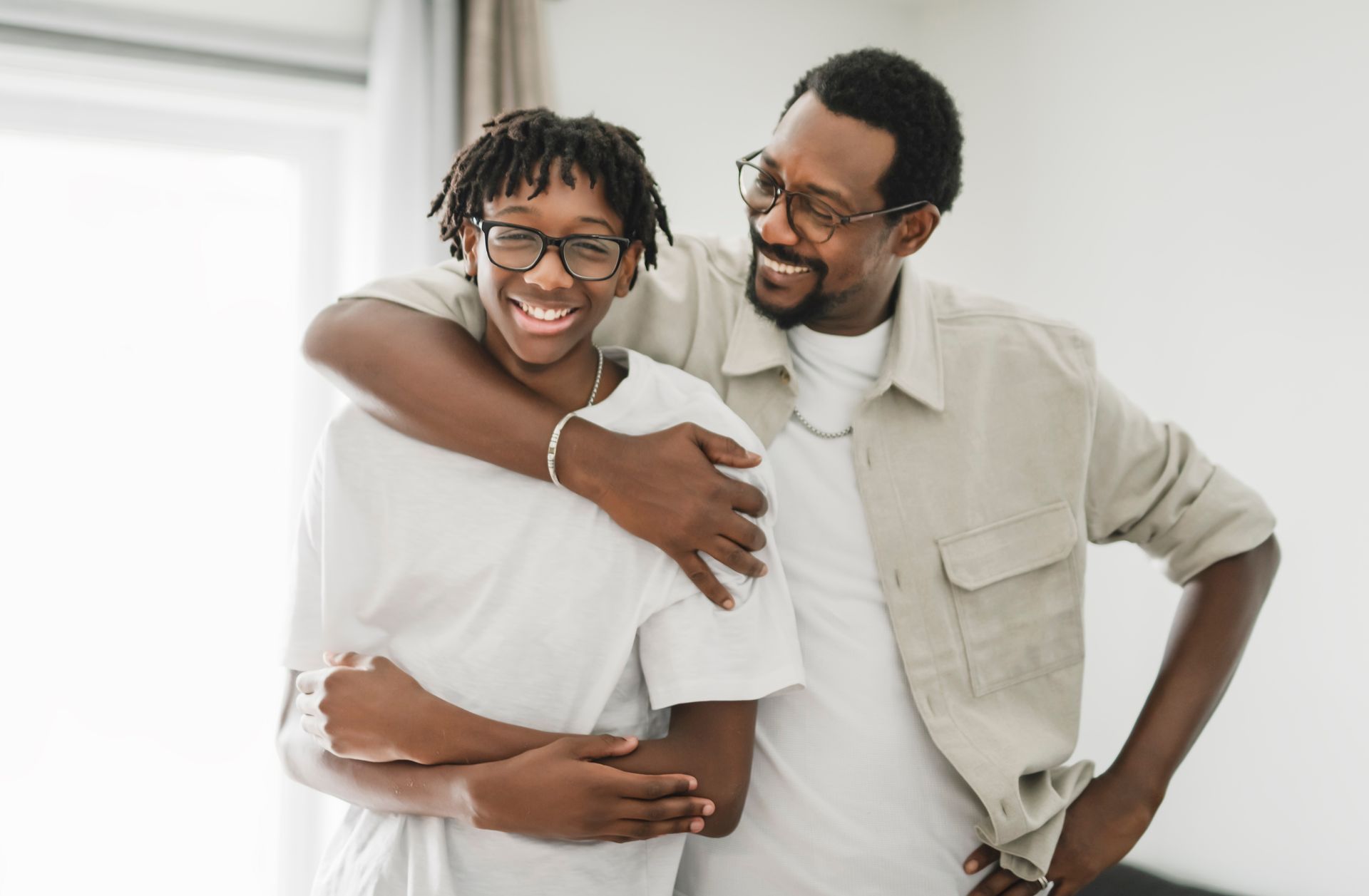 Two smiling people in white shirts embrace in a bright room