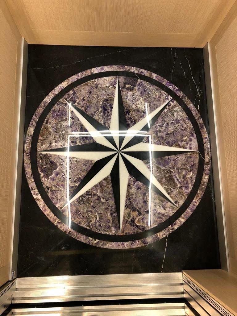 Mosaico circolare a forma di rosa dei venti nei colori nero, bianco e rosa all'interno di un ascensore o di un involucro a forma di scatola.