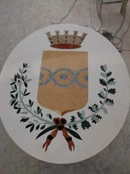 Emblema circolare bianco con scudo coronato e rami di alloro.