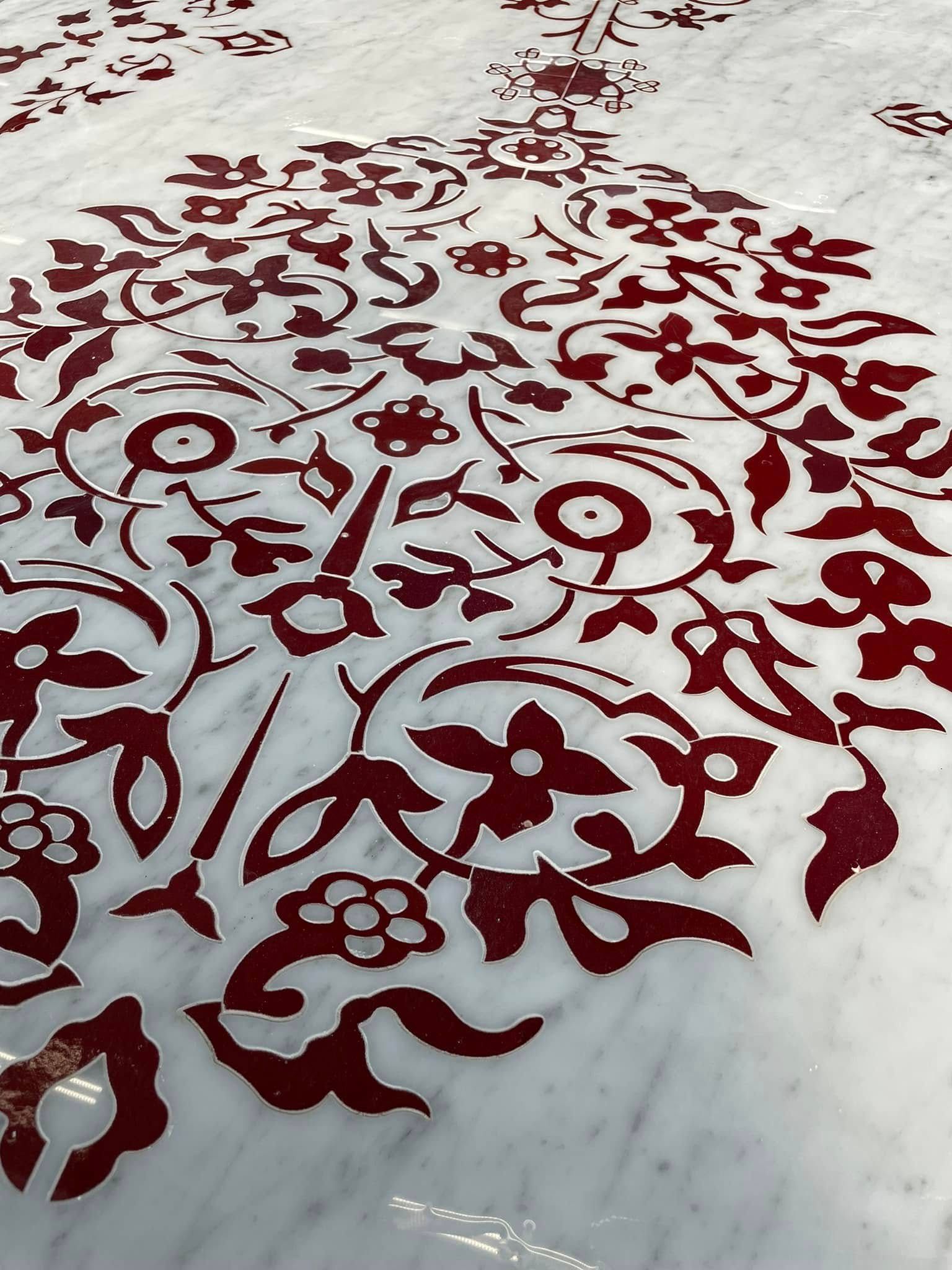 Tappeto rosso con motivo floreale su un pavimento di marmo chiaro, visto dall'alto.