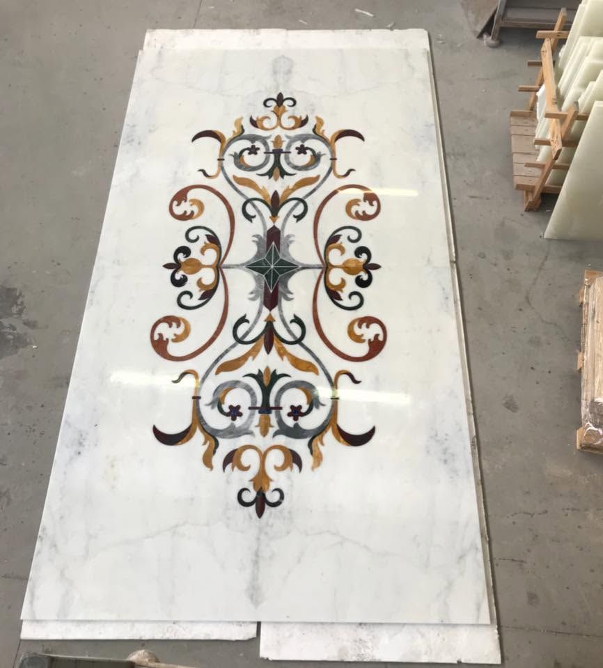 Intarsio floreale decorativo multicolore al centro di una lastra di marmo bianco in un laboratorio.