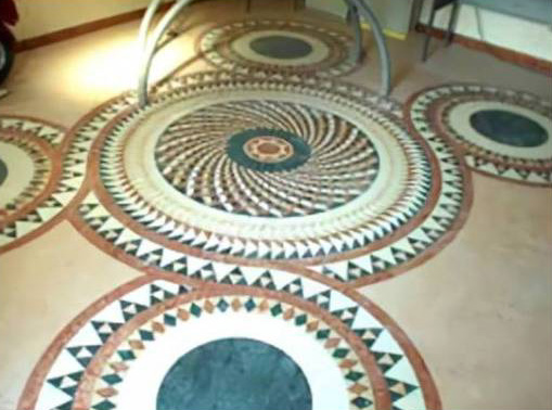 Elegante pavimento a mosaico circolare con motivi geometrici nei toni del verde, del bianco e del terracotta.