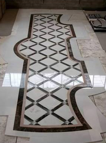 Pannello decorativo per pavimento in marmo bianco con griglia a rombi neri e bordo curvo marrone in un interno piastrellato.