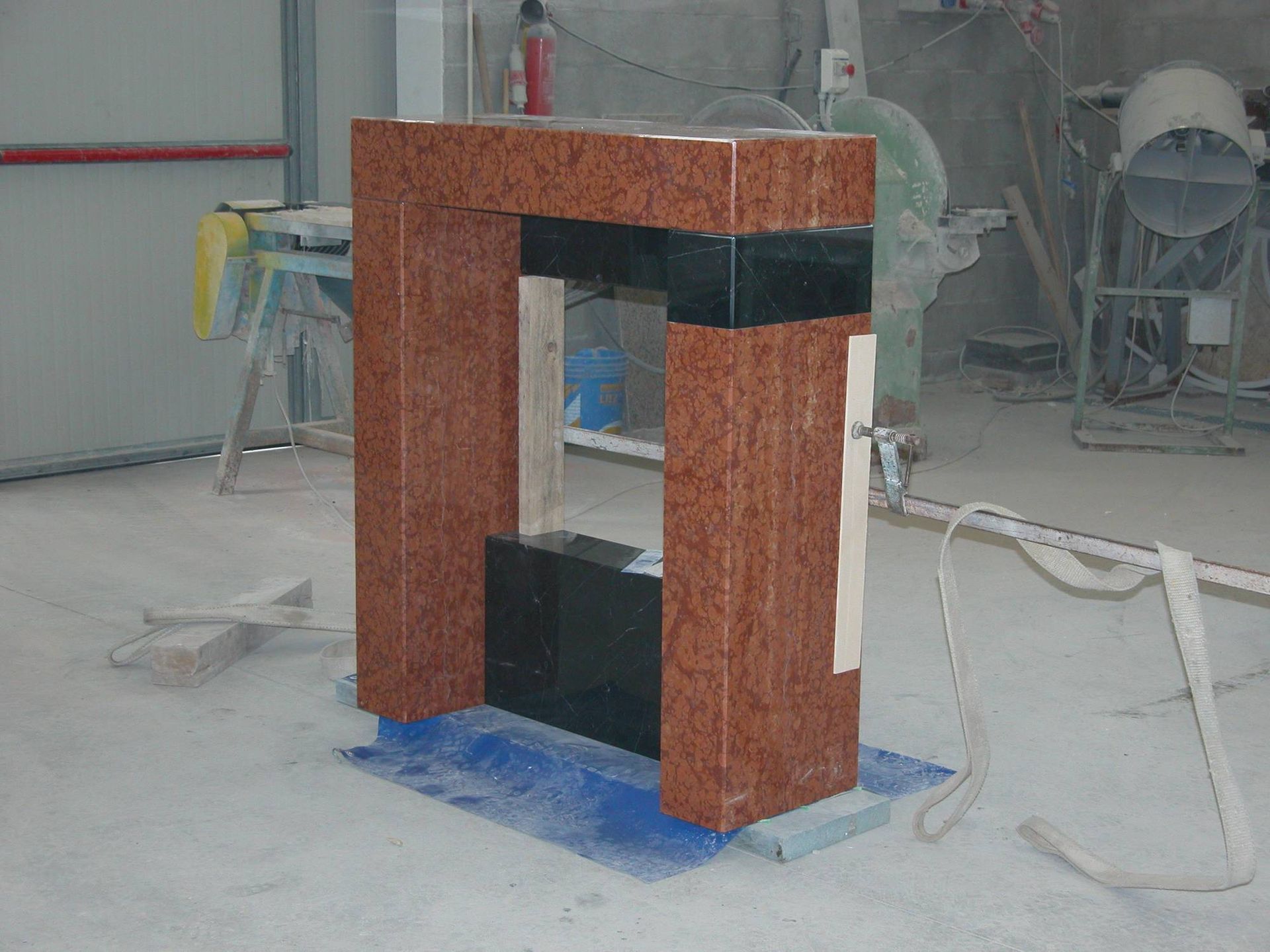 Un piccolo armadietto o chiosco rosso e nero non rifinito in un'officina polverosa, circondato da attrezzi e attrezzature.