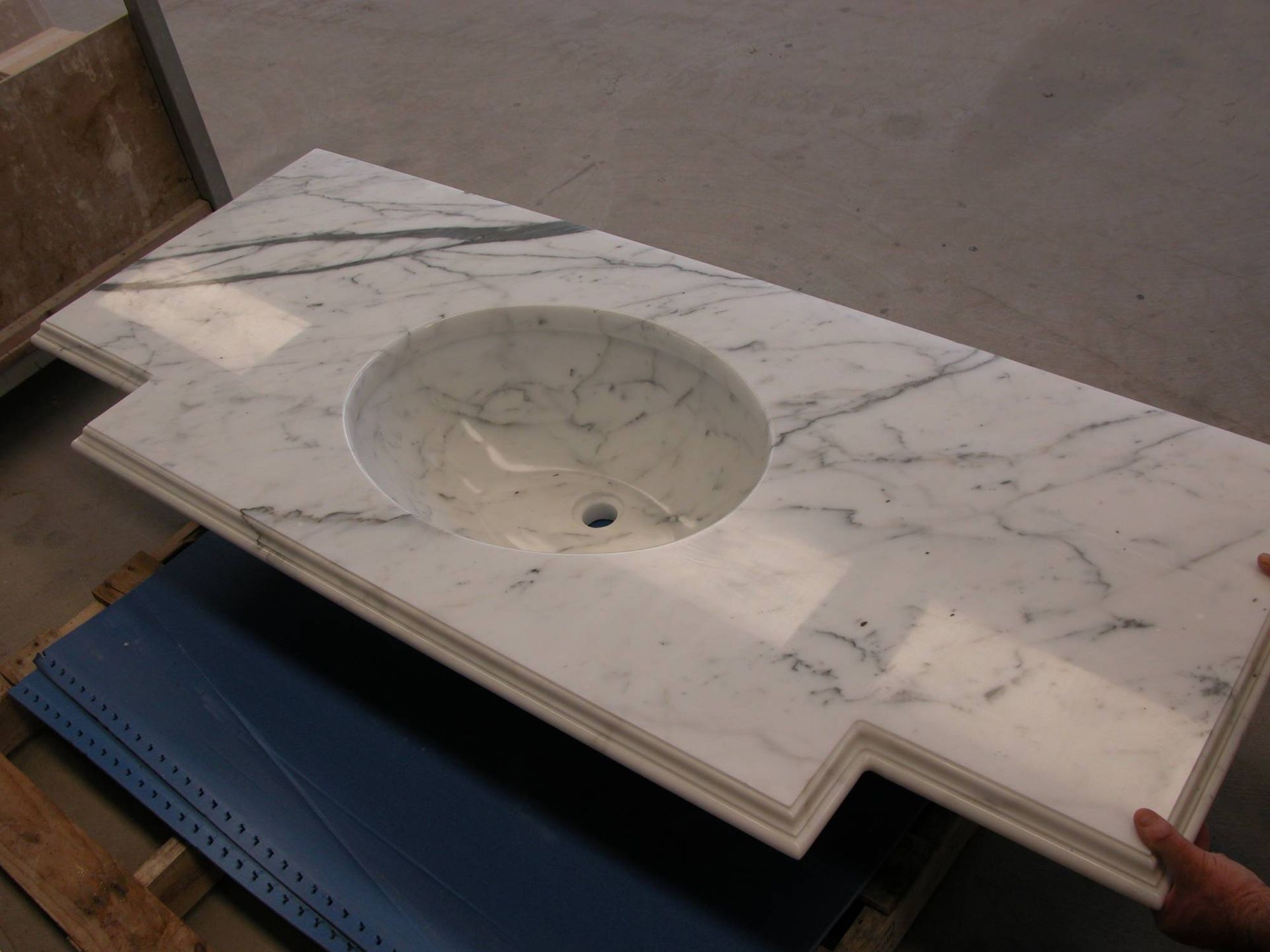 Piano lavabo in marmo con lavabo rotondo integrato e foro per rubinetto, poggiato su un carrello blu.