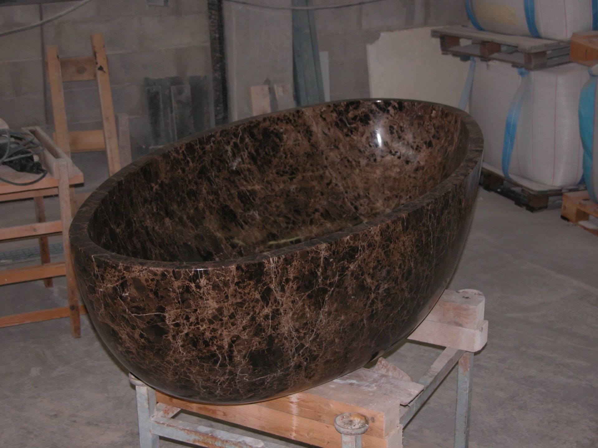 Vasca da bagno in pietra marrone scuro posizionata su un supporto in un'officina o in uno showroom.