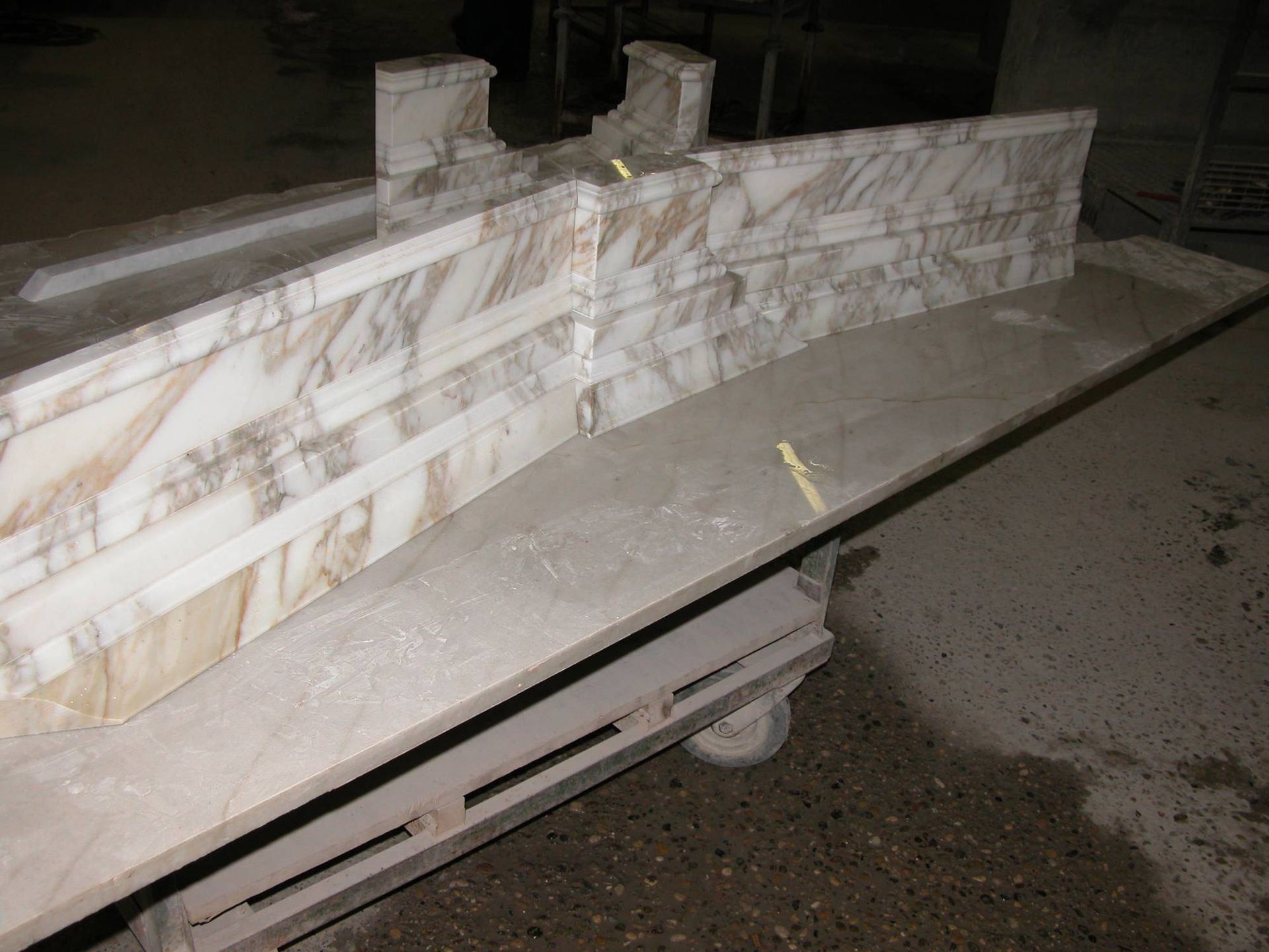 Piano di lavoro in marmo su un carrello con ruote all'aperto di notte, con lastre di pietra bianca e uno sfondo di pavimentazione scura.