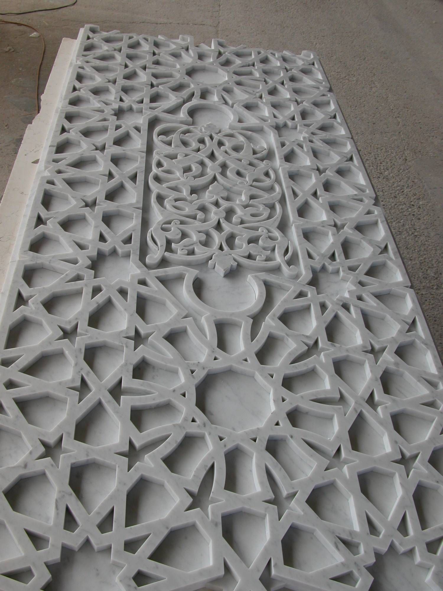 Pannello metallico bianco a griglia con motivi floreali e geometrici intagliati, visto di profilo su un pavimento.