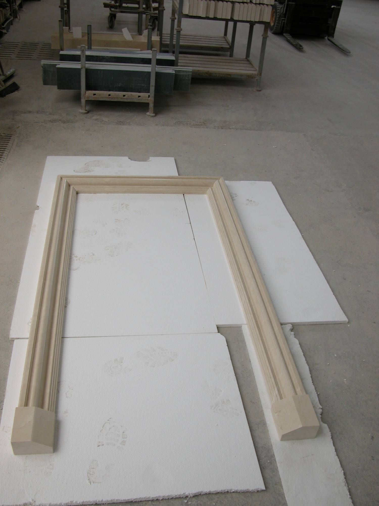 In un'officina, inquadrature di legno disposte su pannelli di polistirolo bianco, con carrelli sullo sfondo.