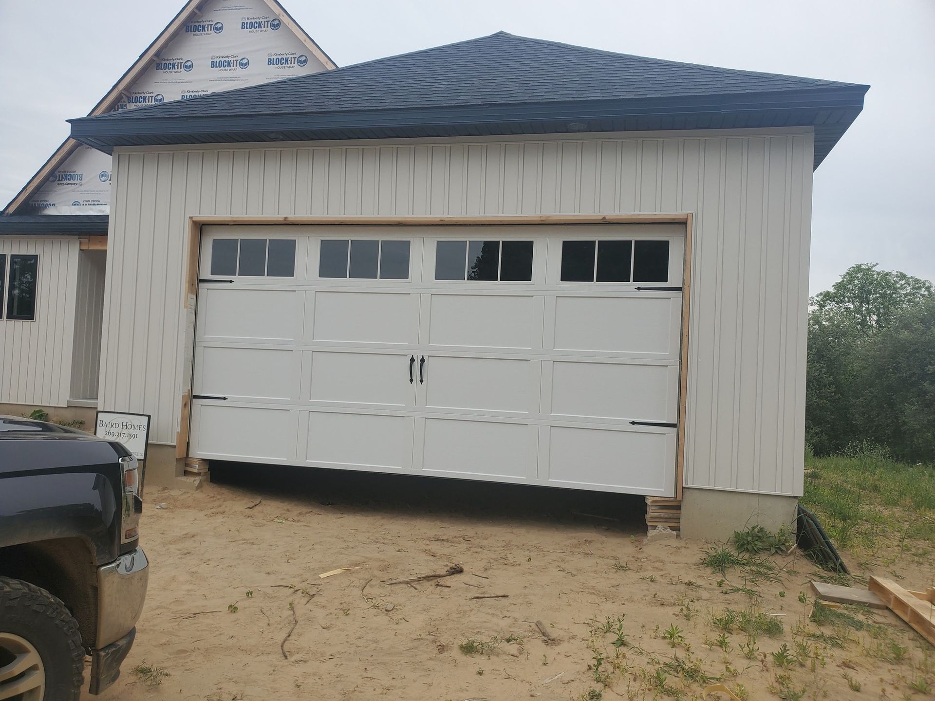 White garage with closed double doors and blue roof beside a dirt driveway under cloudy sky