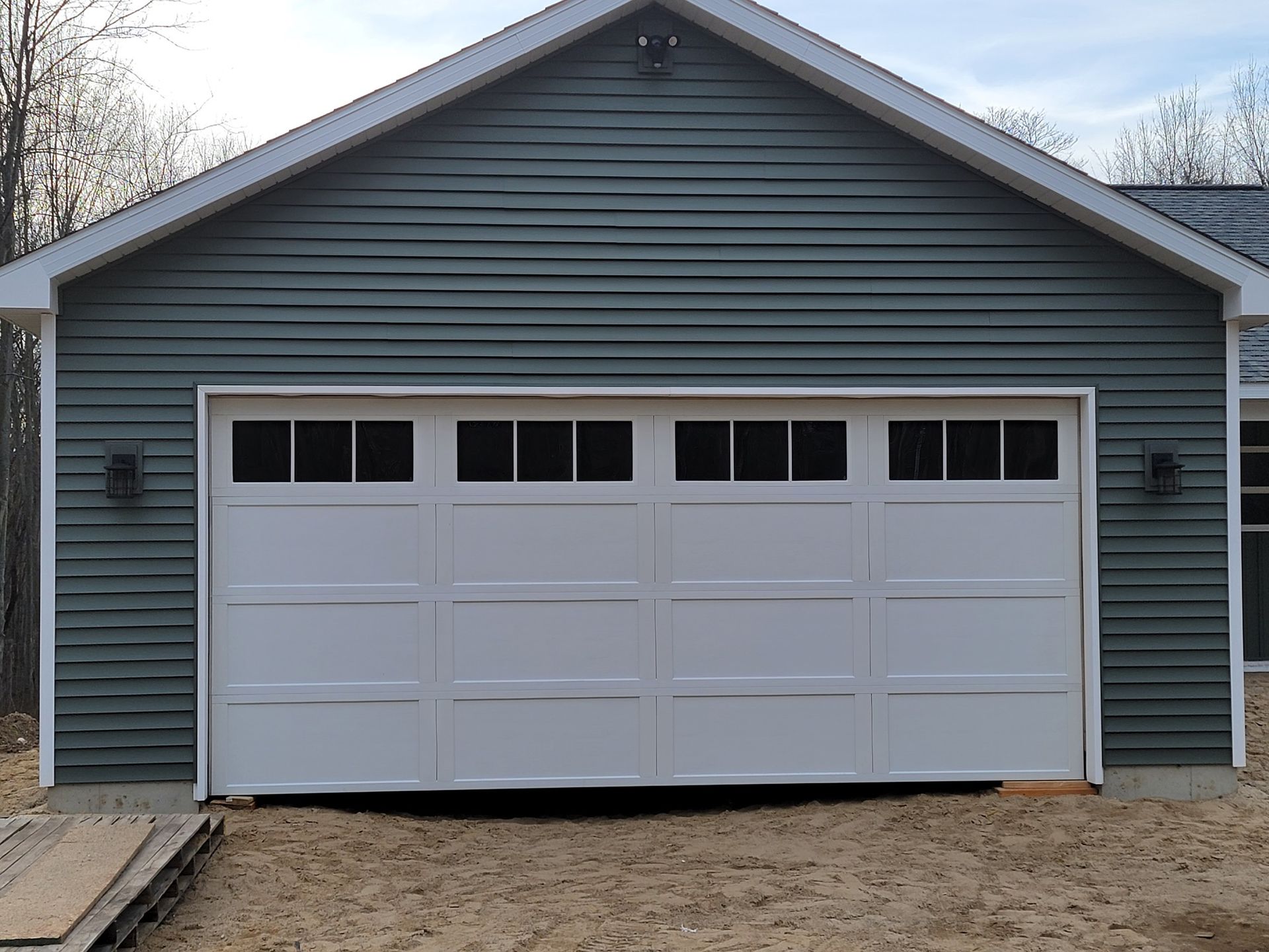 White double garage door on a blue house with a peaked roof and small windows near the top