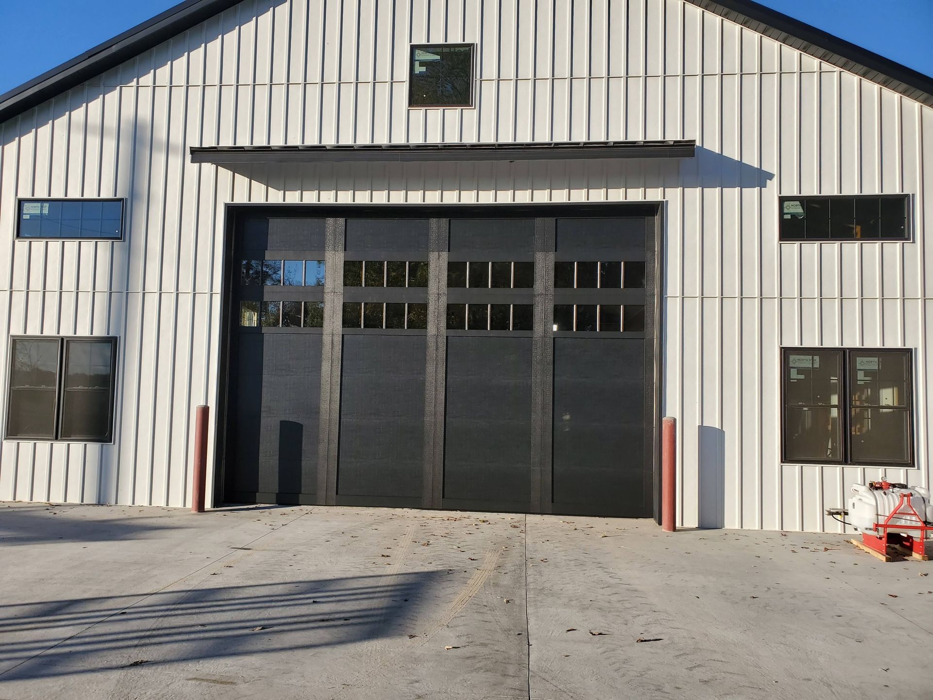 White metal building with a large black garage door and small windows, viewed from the front.