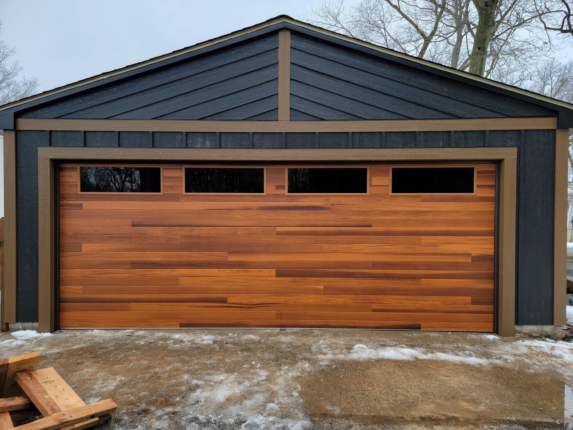Modern house front with a large wooden garage door and dark siding in winter.