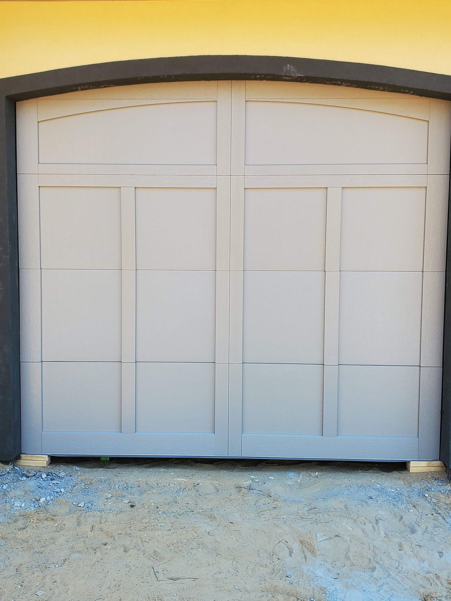 White double garage door with two arched panels on a gray wall above a gravel driveway
