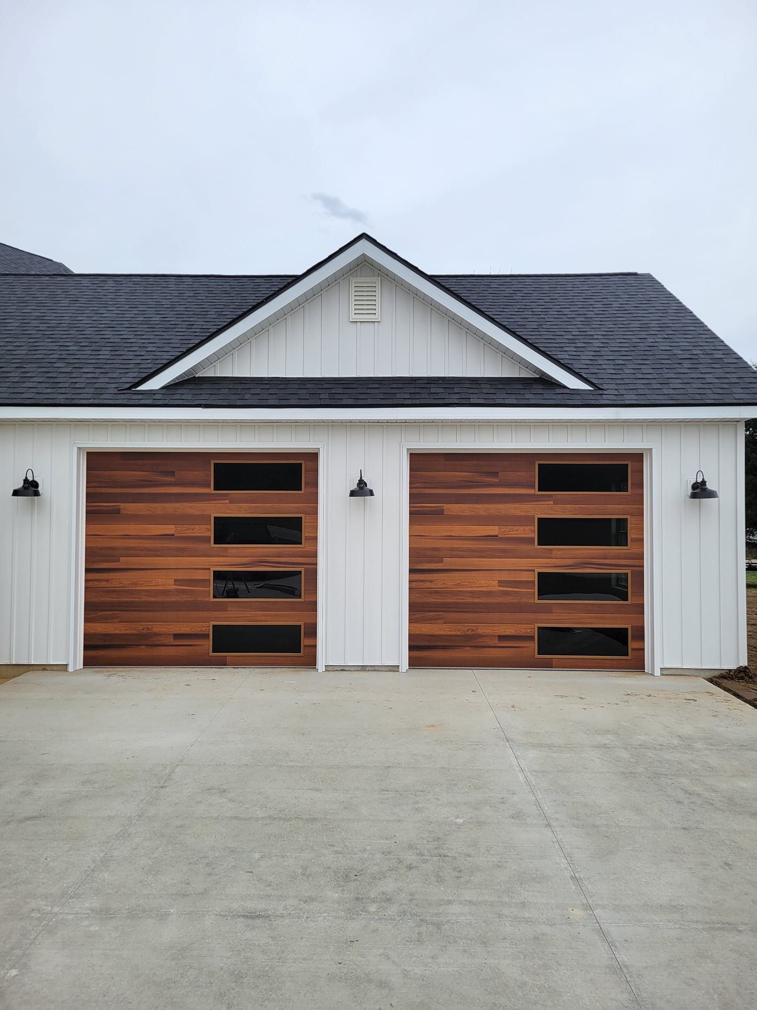 White garage with two wood-paneled doors and dark roof on a concrete driveway