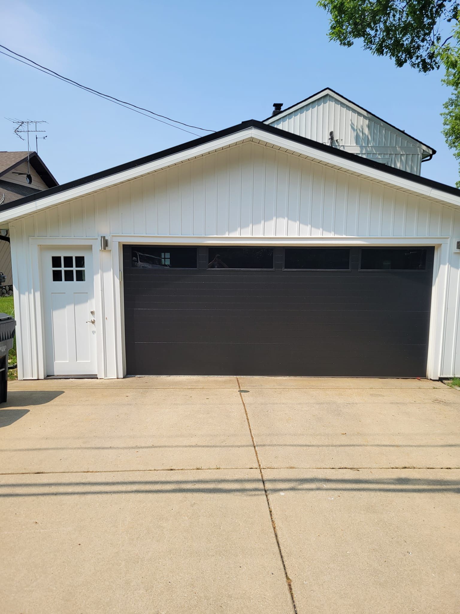 White garage with black door and side entrance beside a concrete driveway under a blue sky