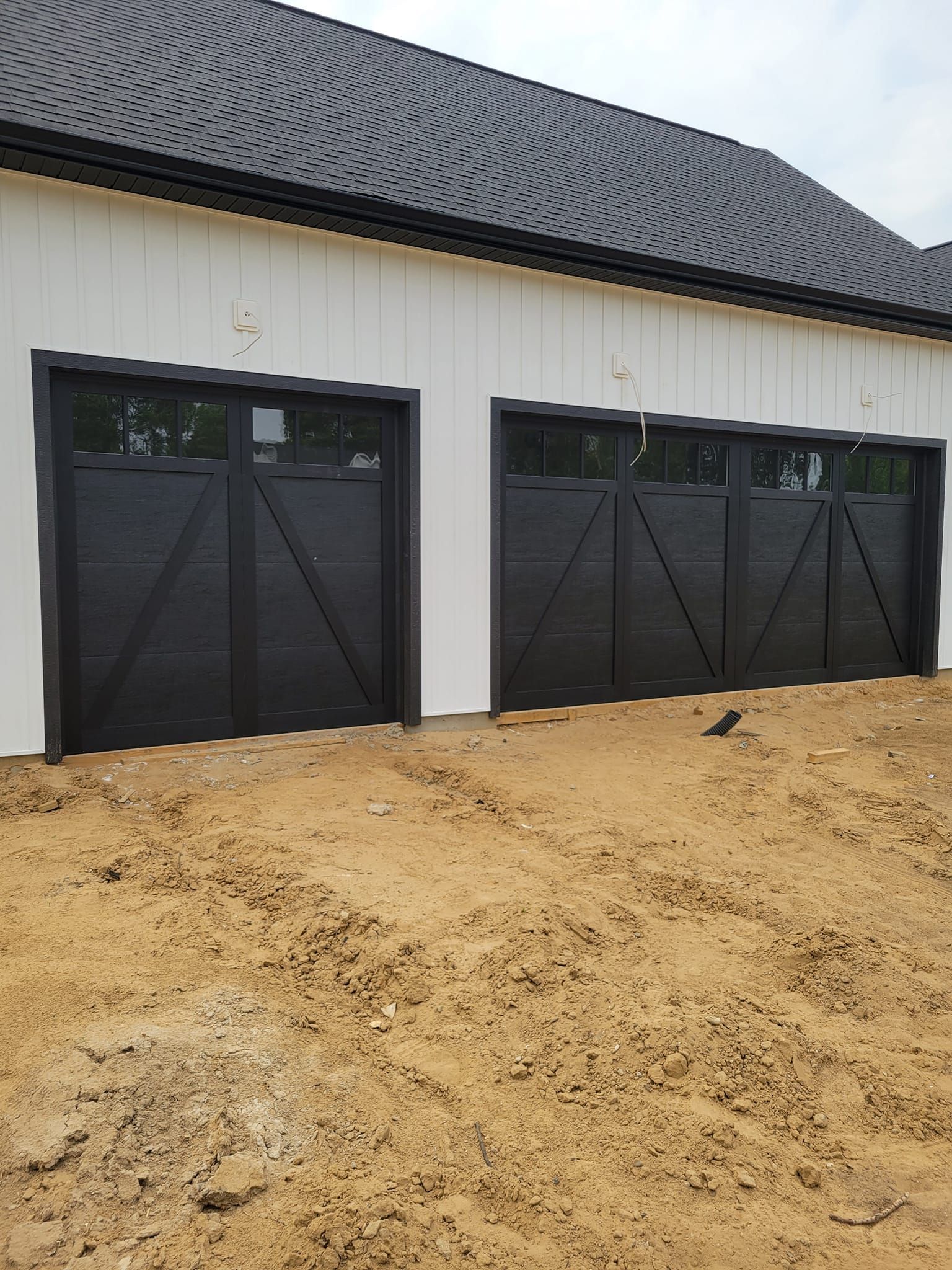 White barn exterior with three black doors and a dirt foreground